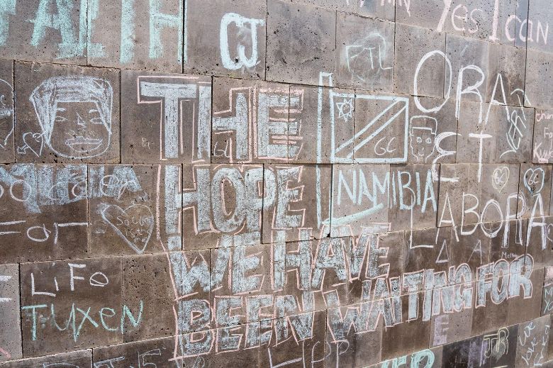Nahaufnahme einer Steinwand mit Kreideschriften, unter anderem „The hope we have been waiting for“